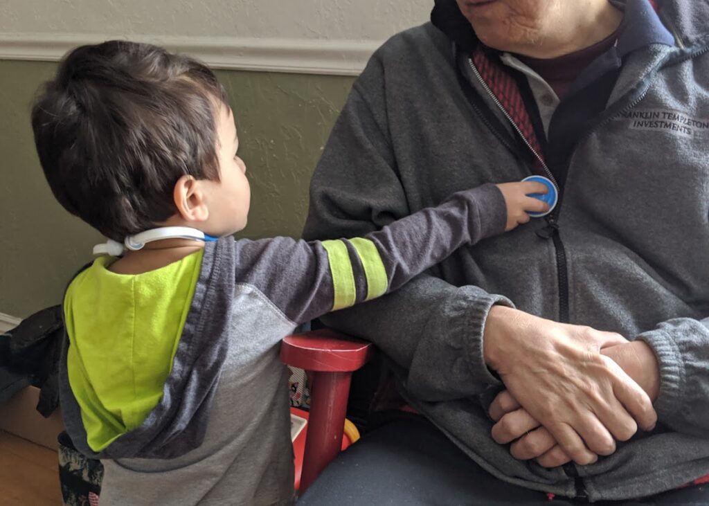 Child using a play stethoscope to try to listen to a man's heart