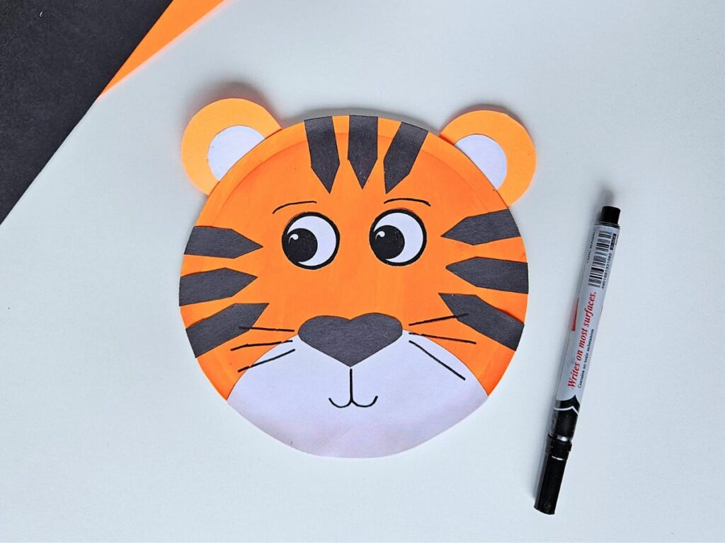 Drawing the whiskers and mouth on a paper plate tiger.