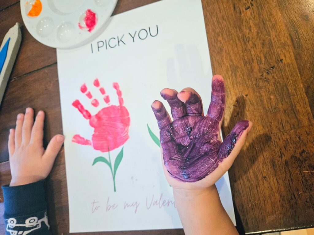 Child's hand covered in paint doing a Valentine's Day handprint craft